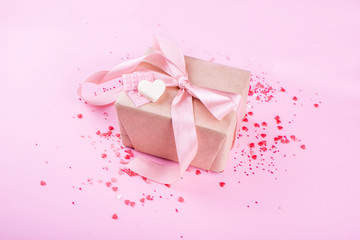 Gift with satin ribbon with small roses on a pink background. Hearts, festive content. Valentine's Day.