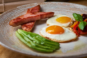 plate of fried eggs with bacon and avocad on wooden table. English breakfast on table
