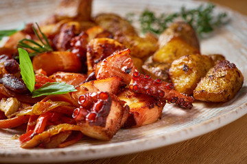 grilled octopus dish with small potatoes and vegetable salad. close up slices of fried octopus on a plate