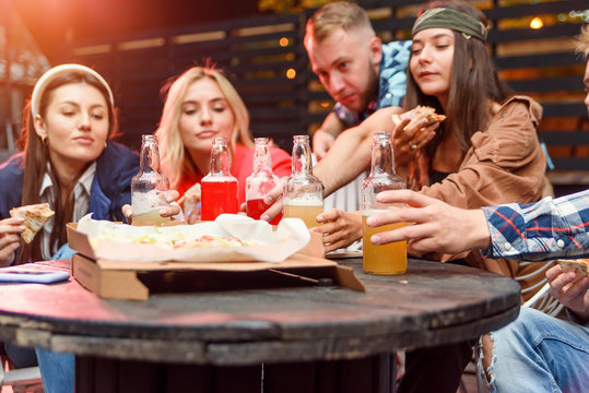 Multi-ethnic friends enjoying pizza and beer in party. Young people having a party. Selective focus on bottles of energy drinks at table.