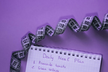 Measuring tape and notepad on lilac background. Weight loss concept