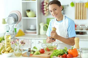 Obraz na płótnie Canvas Cute boy preparing salad on kitchen table at home
