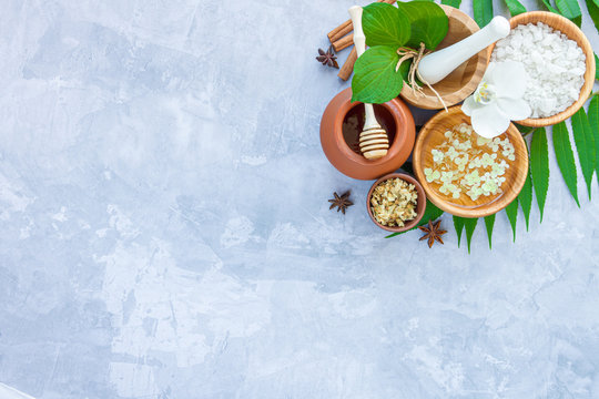 Top view of set for relaxing healing thai spa treatments. Wooden mortar  pounder with herbs, honey pot, flower water and spices are on grey cement  concrete background. Ayurveda salon concept. Stock Photo |