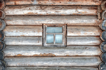 The wall of an old wooden house made of logs with a window.