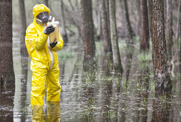 technician in protective coveralls taking  sample of water in plastic  container in floods...