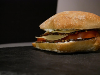 Sliced bread, cheese and ham on black plate and grey background