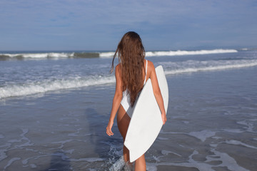 Beautiful young girl with a surfboard on the ocean.