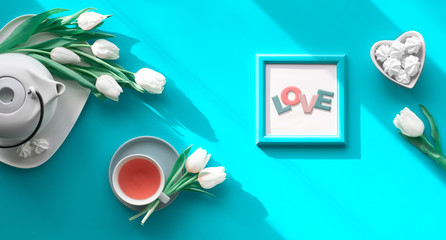 Spring geometric flat lay. Female hand hold frame with text You are special. Tea cup, pot, sweets and white tulips on turquoise. Mothers day, international women day 8 March or your Mom birthday.