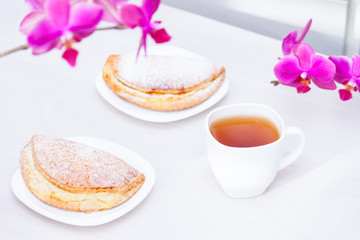Cup of tee, flowers, homemade buns with cottage cheese on white wooden background. Happy day, good morning concept.