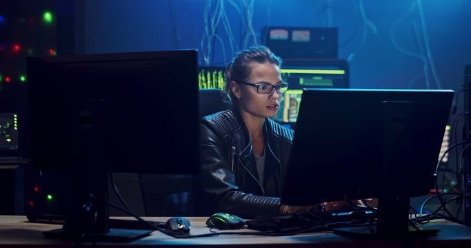 Young Caucasian pretty girl hacker in glasses working at the computer at night and hacking a program so being very happy and cheerful as she managed to get god result.