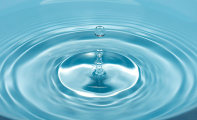 a drop of water falls with a splash into clear, blue water forming circles on the water