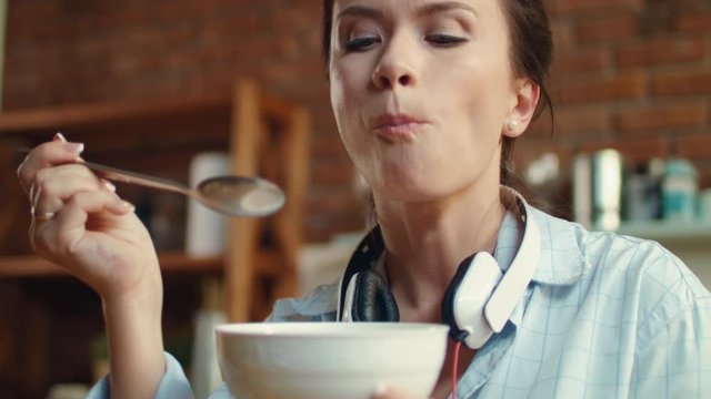 Woman eating cornflaces with milk in kitchen. Girl enjoying cereal for breakfast