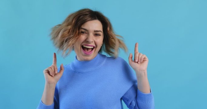 Portrait of a happy smiling young sexy girl listening to music dancing and waving her hands rhythmically in blue sweater on an blue background. Pleasure. Emotions of people. Monotone. Blue pantone
