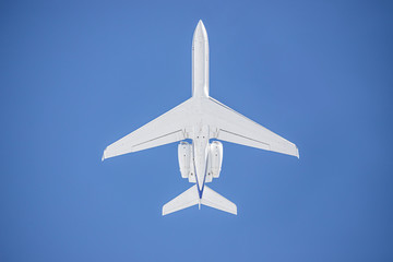 Bottom view of a completely white airplane, an unrecognized commercial airline.