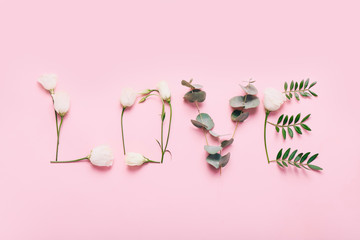 Word LOVE made of flowers and leaves on pink background.