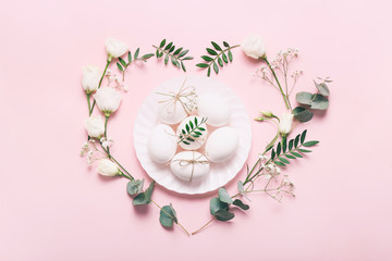 White Easter eggs with flowers and green leaves on pink background