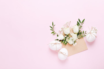 White Easter eggs and envelope with flowers and green leaves on pink background