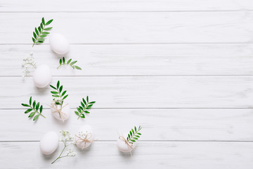 White Easter eggs with flowers and green leaves on white wooden background