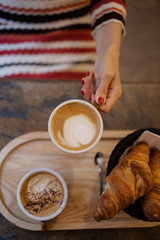 Morning breakfast in a cafe with a cup of coffee in hand and a warm croissant in a plate on a wooden tray.