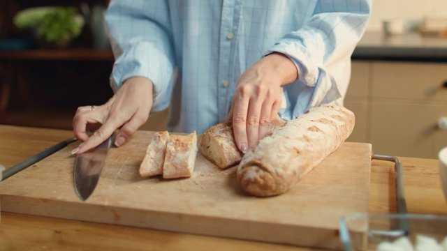 Woman hands slicing bread. Brunette female eating baguette in kitchen.