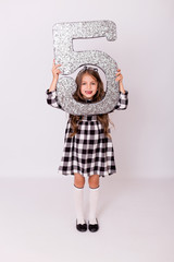 Little child girl in dress posing with silver 5 number isolated over white background. Caucasian girl shows her tongue in funny grimace.