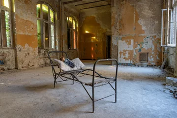 Foto op Plexiglas oude vuile verlaten kamer met een stalen bedframe en een oude pop op een kussen © Peter Jesche
