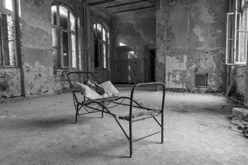 Foto op Plexiglas zwart-wit, oude vuile verlaten kamer met een stalen bedframe en een oude pop op een kussen © Peter Jesche