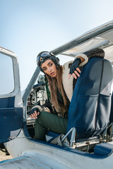 the girl the pilot sits looks at the end of the plane from the cockpit with the side panel on his head, the pilot's helmet and glasses