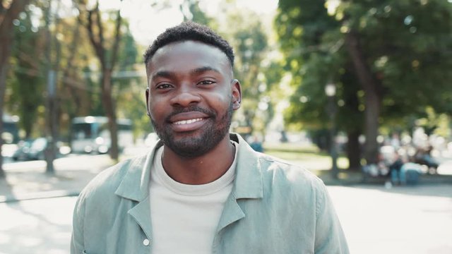 Portrait of attractive cheerful african american man stands in city street smile happy sunset young attractive face positive sunlight city fashion outdoor close up slow motion