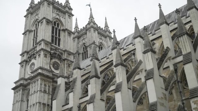 View from the bottom on the Westminster Abbey exterior details against the grey cloudy sky. Action. It is a large, mainly Gothic abbey church in the City of Westminster, London