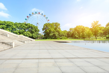 Empty square floor and green forest with playground ferris wheel. - Powered by Adobe