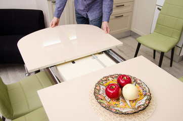man spreads a sliding glossy dining table on which stands a plate with artificial fruit