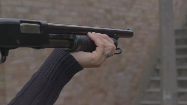 Side view of a person aiming a pump action shotgun with a folding stock
