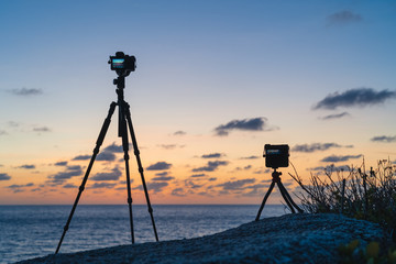 Two cameras standing on a tripods on the beach against the background of dawn