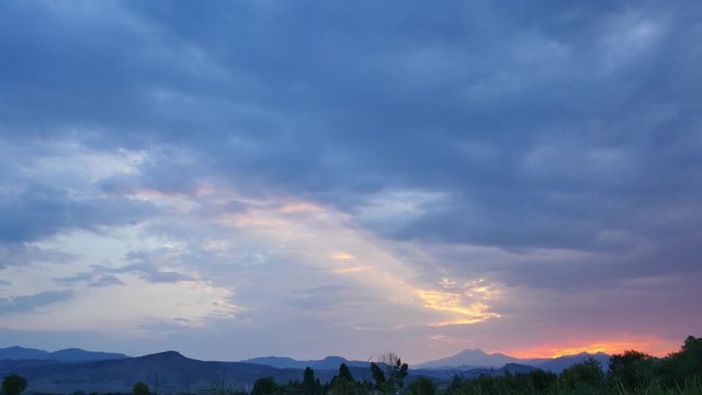 Extreme wide establishing shot of blue clouds and a sunset over a green field with the rocky mountains in the distance