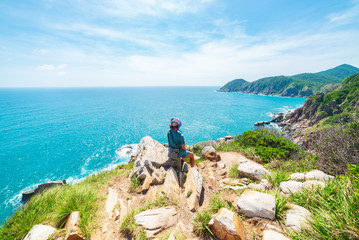 Woman looking at tropical coast from cliff above. Vietnam travel destination, Phu Yen province between Da Nang and Nha Trang. Gorgeous rocky coastline blue waving sea rock boulders,