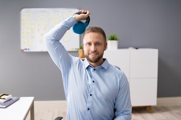 Young Businessman Exercising With Kettlebell In Office