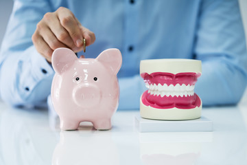 White Tooth Beside Man Inserting Coin In Piggy Bank