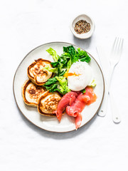 Delicious healthy brunch - poached egg, smoked salmon, green salad and savory pancakes on a light background, top view