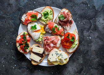 Variety of aperitifs sandwiches plate - sandwiches with prosciutto, avocado, salmon, egg, tomatoes,...