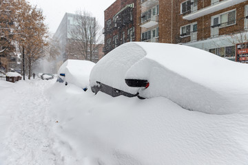 Snow covered cars parked on side of road in a Montreal neighborhood with man walking in the distance 