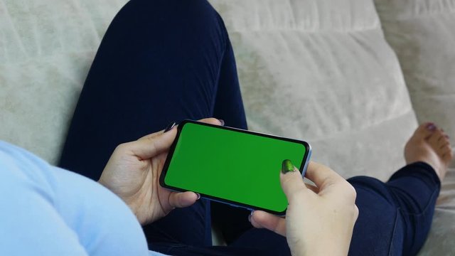 Woman at home relaxing reading on the smartphone with pre-keyed green screen
