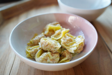 Pork wonton in pink&white bowl. On wood table.