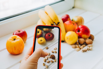 Shooting healthy food content on a smartphone. Man's hand holds a smartphone takes off fruits and nuts. The concept of a healthy lifestyle, proper nutrition, organic food. Raw food diet. Veganism 
