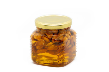 Glass jar with honey and almonds on white background