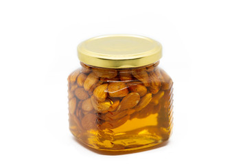Glass jar with honey and almonds on white background