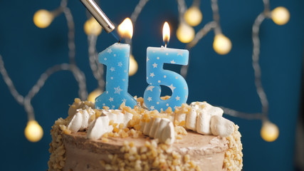 Birthday cake with 15 number candle on blue backgraund set on fire by lighter. Close-up