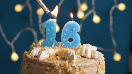 Birthday cake with 16 number candle on blue backgraund set on fire by lighter. Close-up