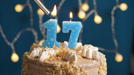 Birthday cake with 17 number candle on blue backgraund set on fire by lighter. Close-up