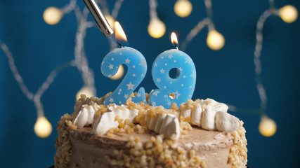 Birthday cake with 29 number candle on blue backgraund set on fire by lighter. Close-up